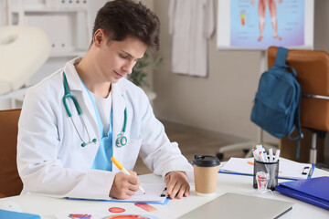 Wall Mural - Male medical intern writing at table in clinic