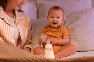 Sticker - Mother with bottle of milk and her little baby in bedroom at night, closeup