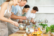 © JackF - Positive interested young woman attending group culinary classes, standing by table with ingredients and utensils, learning culinary skills from professional chef