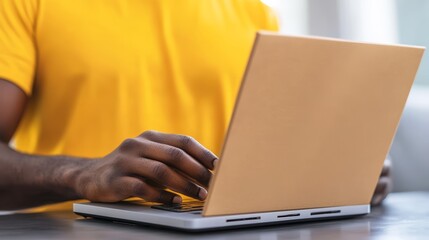 Person using laptop with yellow shirt, modern workspace.