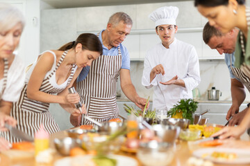 Pleasant and sociable young man, professional chef, leading culinary courses, imparting cooking skills to diverse group of people of different ages