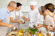 © JackF - Smiling middle-aged man cook conducting culinary classes for learners standing around kitchen table with whisk and bowl in hands