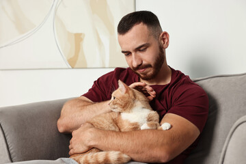 Canvas Print - Man petting cute ginger cat on armchair at home