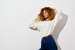 © SHOTPRIME STUDIO - Fashion portrait of a young woman with curly hair wearing a stylish white sweater and high waisted jeans against a minimalist white background