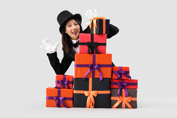 Sticker - Young Asian woman dressed as magician with Halloween gifts on light background