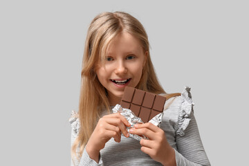 Wall Mural - Cute little girl with sweet chocolate bar on grey background