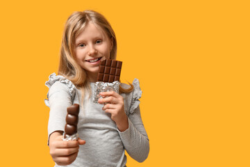 Wall Mural - Cute little girl with sweet chocolate on yellow background