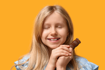 Canvas Print - Cute little girl with sweet chocolate on yellow background