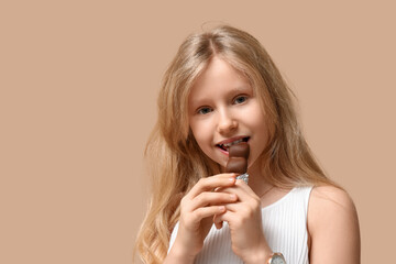 Canvas Print - Cute little girl eating sweet chocolate on brown background