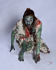 Canvas Print - portrait of scary female model wearing spooky halloween costume, ripped clothes and fake blood like an undead demon apocalyptic zombie character. Isolated figure, crawling poses dark studio background