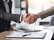 © tiantian - A photograph of two people shaking hands over an open job application on the desk. One person is wearing a grey suit and the other a black shirt. A laptop is visible in the background. This is a stock