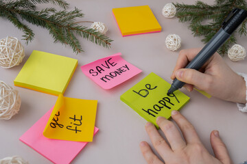 Female hands writing handwritten new year resolutions aims goals on sticky notes. Preparation for New Year. Concept of planning and setting goals for personal development 