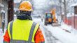 © Nattapol - construction worker in bright orange safety jacket and hard hat stands in snow, observing worksite. scene captures challenges of winter construction, highlighting workers dedication