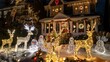 © suteeda - A night-time exterior view of a house covered in festive holiday lights and decorations, including illuminated reindeer and snowmen on the lawn