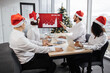 © sofiko14 - Happy team of diverse business people in Santa hats listening their middle aged male bearded chief, showing dynamics of r world market, using digital TV screen at office decorated with Christmas tree.