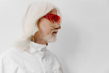 Wall Mural - Fashionable elderly man with white hair and red sunglasses against a minimalist white background, showcasing modern style and personality in a creative portrait setting