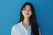 © Surachetsh - Beautiful Asian girl with long dark hair stands smiling warmly in front of a turquoise background. She is wearing a simple white shirt, exuding natural beauty and positivity.