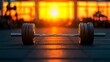 © Chananporn - Barbell resting on gym floor during sunset with vibrant orange and yellow hues.