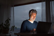 © Halfpoint - Handsome man working from home office at evening, using laptop. Screen glow illuminates man's face. Telecommuting and home office.