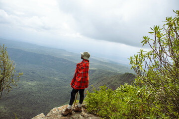 A young black hiker standing on the peak of a mountain looking at the view