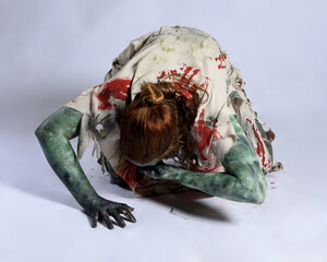 Wall Mural - portrait of scary female model wearing spooky halloween costume, ripped clothes and fake blood like an undead demon apocalyptic zombie character. Isolated figure, crawling poses dark studio background