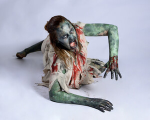 Wall Mural - portrait of scary female model wearing spooky halloween costume, ripped clothes and fake blood like an undead demon apocalyptic zombie character. Isolated figure, crawling poses dark studio background