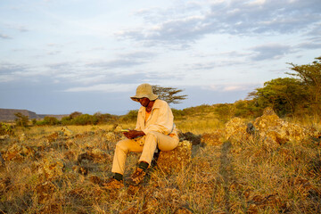 A young black woman sitting on a rock at sunset in a valley countryside