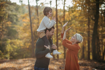 Wall Mural - Young family with small children on walk in autumn forest. Father carrying daughter on his shoulders.