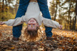 © Halfpoint - Father holding little girl by legs heand down, playing during walk in autumn forest. Dad and girl having fun outdoors.