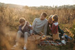 © Halfpoint - Portrait of family having picnic in autumn nature, eating sandwiches, fruits and cheese in the middle of meadow. Young boy taking pictures with vintage camera.