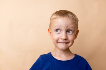 A cheerful young boy with short blonde hair and blue eyes makes a playful expression against a neutral background