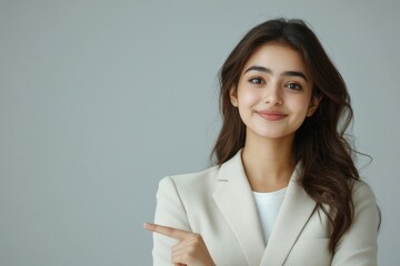 Smiling young adult indian business lady teacher in formal wear white suit looking away and pointing index finger aside. Happy woman standing isolated, Generative AI