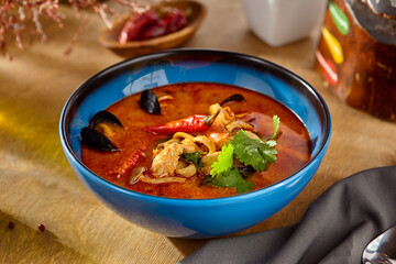 Sticker - Tom Yum Soup with Seafood in Blue Bowl on Wooden Table Garnished with Cilantro and Chili Peppers