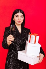 Portrait of a happy young woman with Christmas gifts and a glass of champagne on a red background