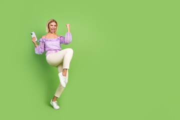 Wall Mural - Photo of crazy cheerful girl wear stylish clothes hand hold modern device empty space isolated on green color background