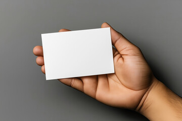 Canvas Print - Close-up of a hand holding a blank white business card against a gray background, showcasing the front side. The card is empty and ready for customization or branding.