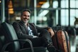 © ChaoticMind - A confident man is seated in an airport lounge with a brown suitcase, wearing a grey blazer and a watch, exuding a calm and composed demeanor while smiling brightly.