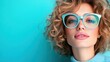 © familymedia - A woman with curly hair wearing stylish glasses poses confidently against a vibrant turquoise background, showcasing modern eyewear fashion in a bold contemporary style.