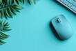 © Natalia - Minimalistic workspace with a teal computer mouse, part of a keyboard, and green leaves on a teal background.
