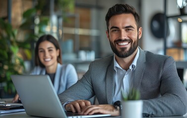 Two business professionals smiling in a modern office setting with laptops and warm lighting