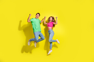 Sticker - Full size photo of two nice young people hold arms jump raise fists isolated on bright yellow color background