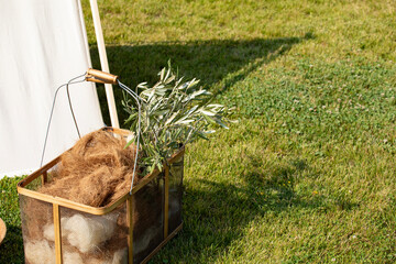 Outdoor wedding decor with olive branches and basket with natural fibers on green grass, copy space