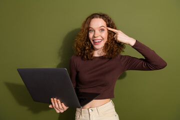 Sticker - Photo of cheerful smart teen lady dressed brown clothes studying modern device finger temple isolated green color background