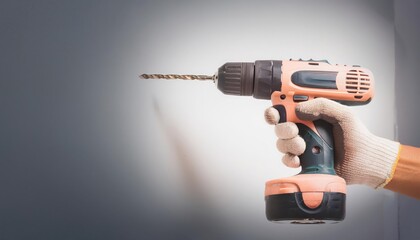 Hand holding a cordless drill with a bit against a wall.