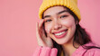 © Alina Tymofieieva - Young woman smiles with colorful makeup and yellow knitted hat against a pink background