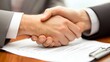 © Galib - Two people shaking hands over a table with a clipboard.