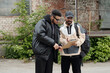 © pressmaster - Two men are standing in front of building, discussing documents on a clipboard. One is wearing a black jacket, while other is in beige jacket and cap, both appear focused on their task