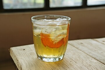 A glass of iced tea with a slice of orange, served on a rustic wooden table. The refreshing drink glistens in the sunlight, offering a thirst-quenching, citrusy, and cool sensation.