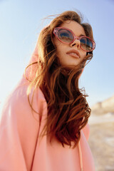 Wall Mural - Stylish woman in pink hoodie and sunglasses standing confidently in the desert