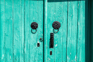 Old turquoise door with black metal door knockers showing weathering